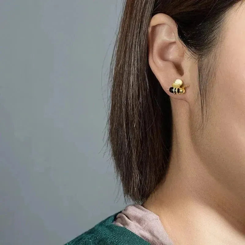 Gold bee-shaped earring worn by a person with a neutral background