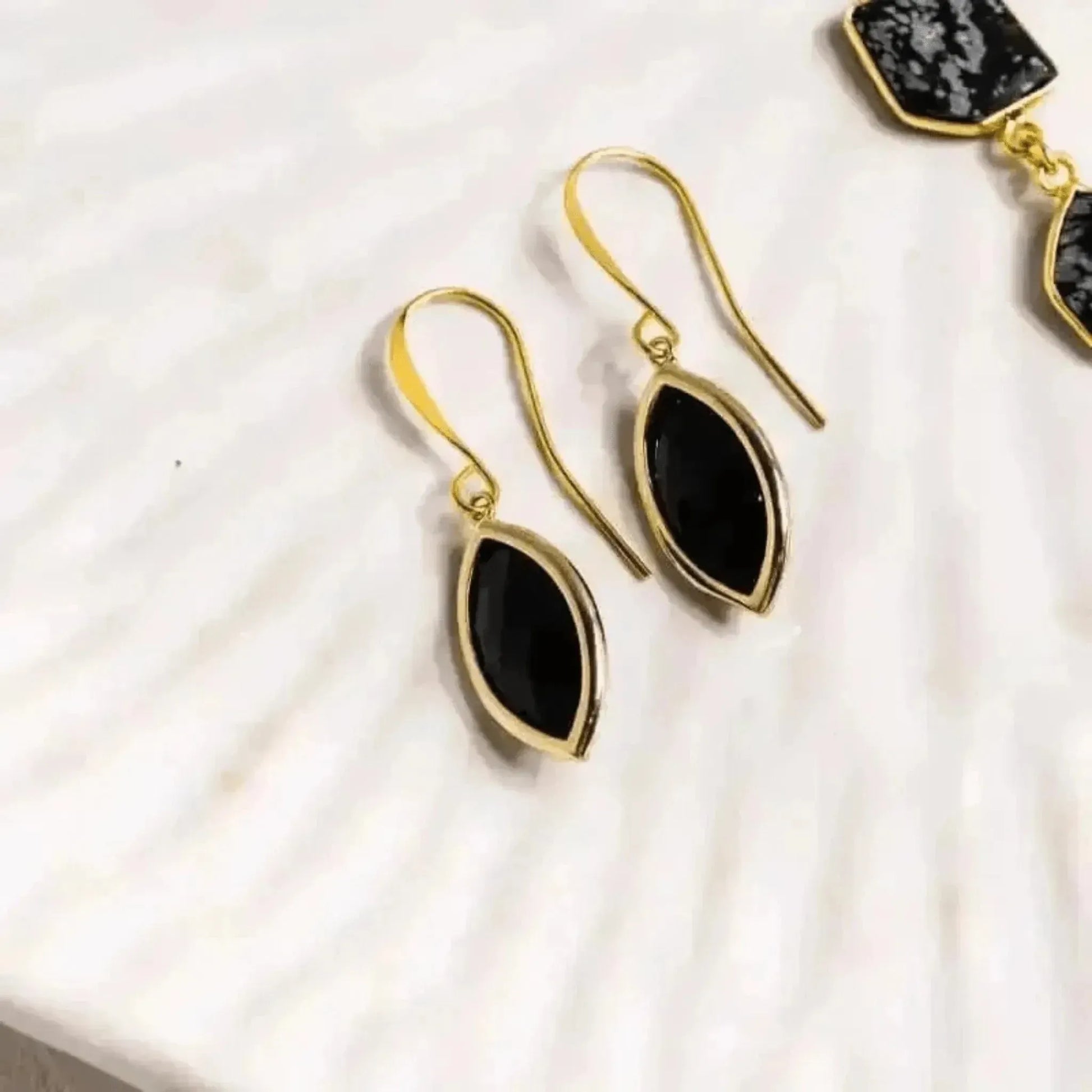 Gold earrings with black stones on a white fabric background