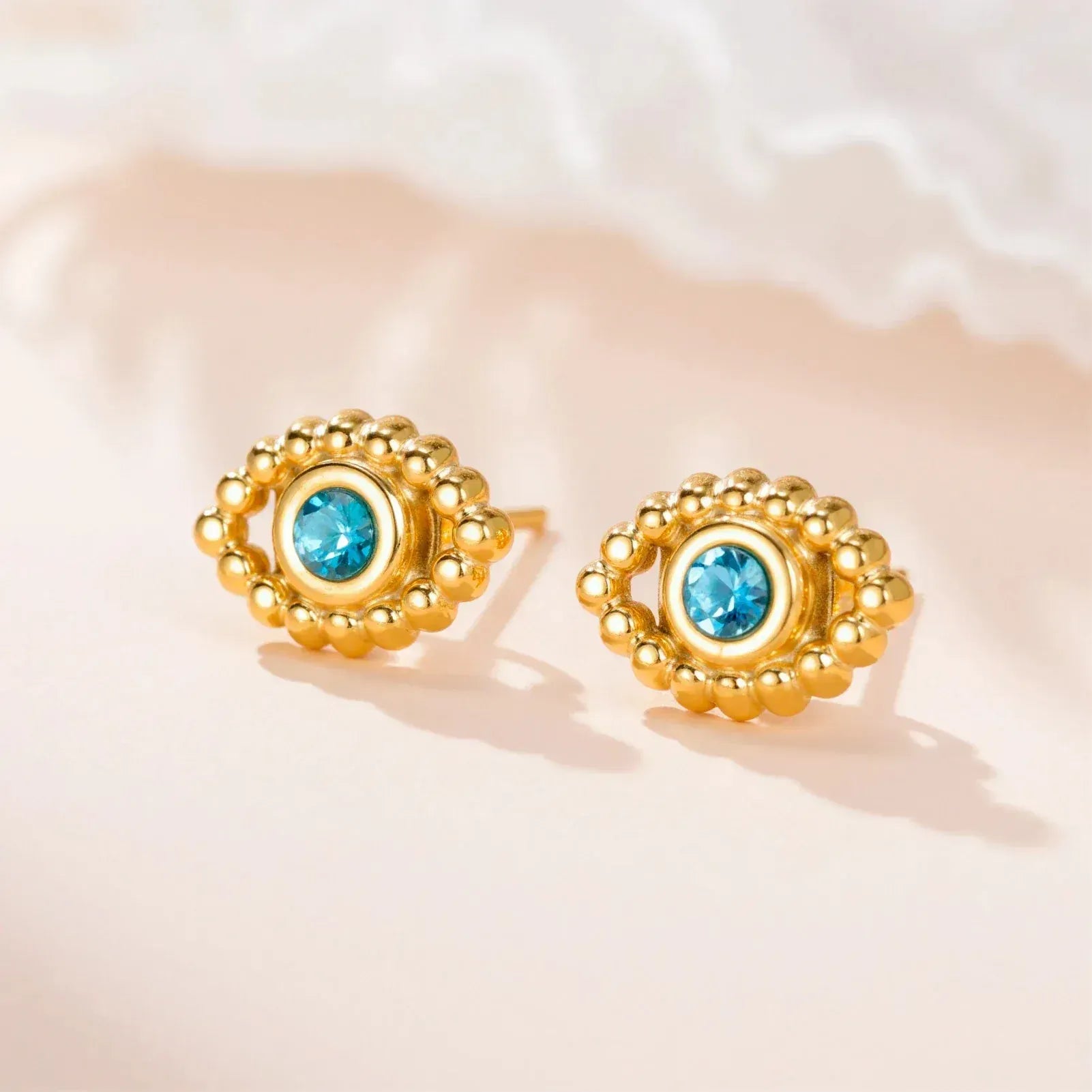 Gold earrings with blue gemstones on a soft pink background