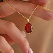 Gold necklace with a red pendant held by a hand against a blurred background