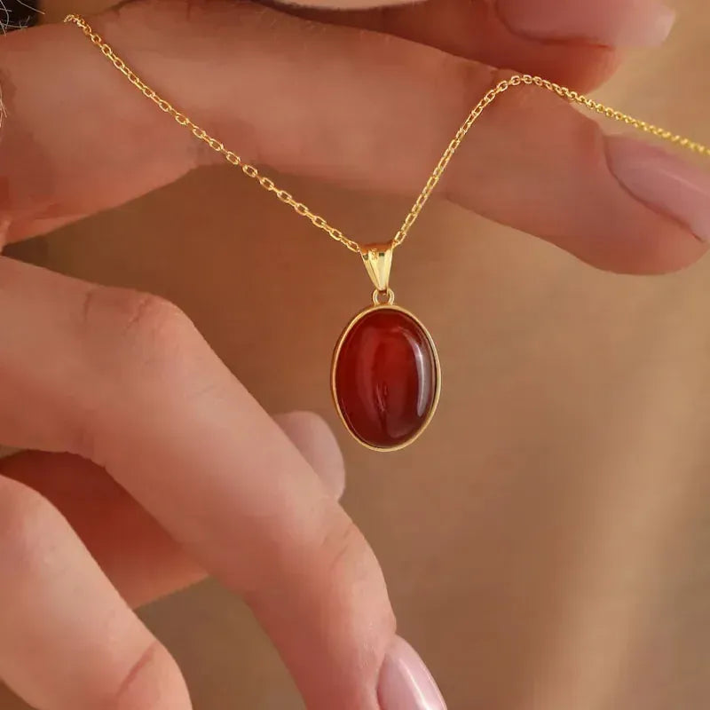 Gold necklace with a red pendant held by a hand against a blurred background