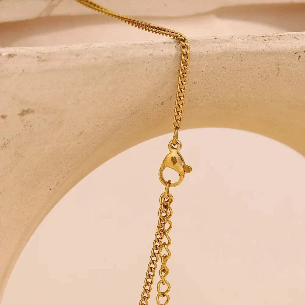Gold chain necklace with clasp on a beige stone surface