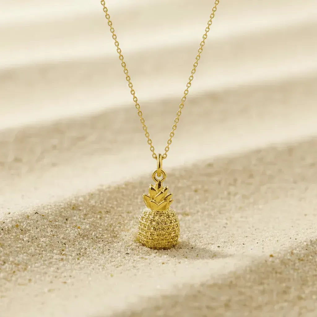 Gold pineapple necklace on a sandy background