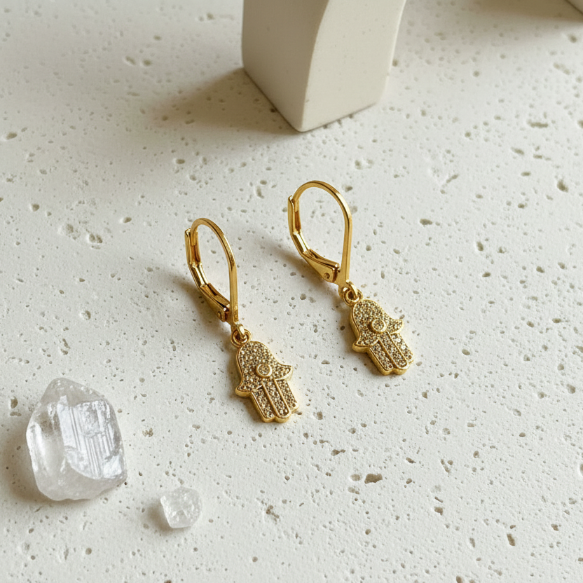 Gold plated crystal hamsa hand earrings with eye detail beside clear quartz