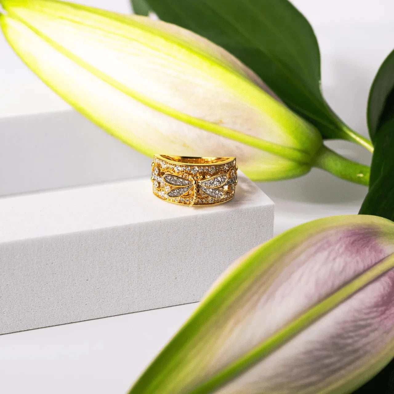 Gold ring with diamond accents on a white surface with green leaves