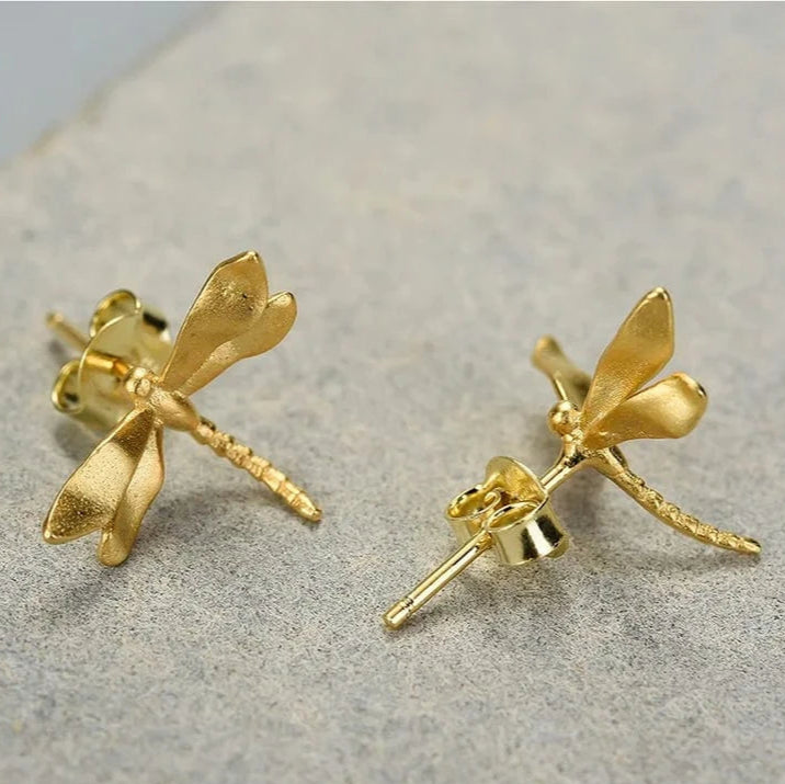 Gold dragonfly-shaped earrings on a textured surface