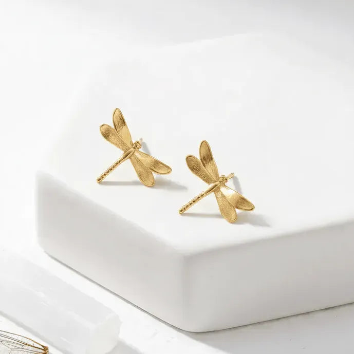 Gold dragonfly earrings on a white surface
