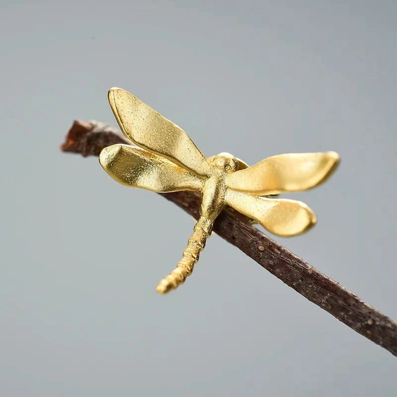 Gold dragonfly figurine on a branch against a gray background