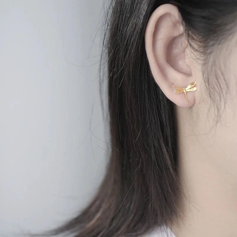 Gold dragonfly earring worn by a person with a neutral background