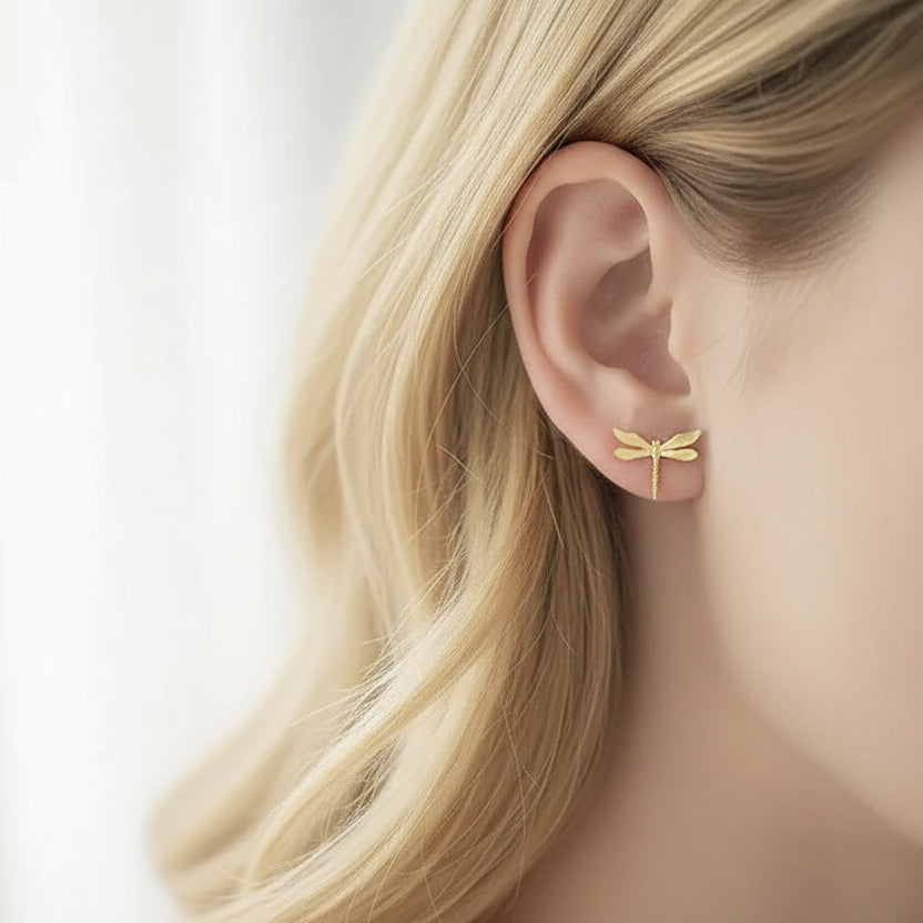 Gold dragonfly earring worn by a person with a neutral background