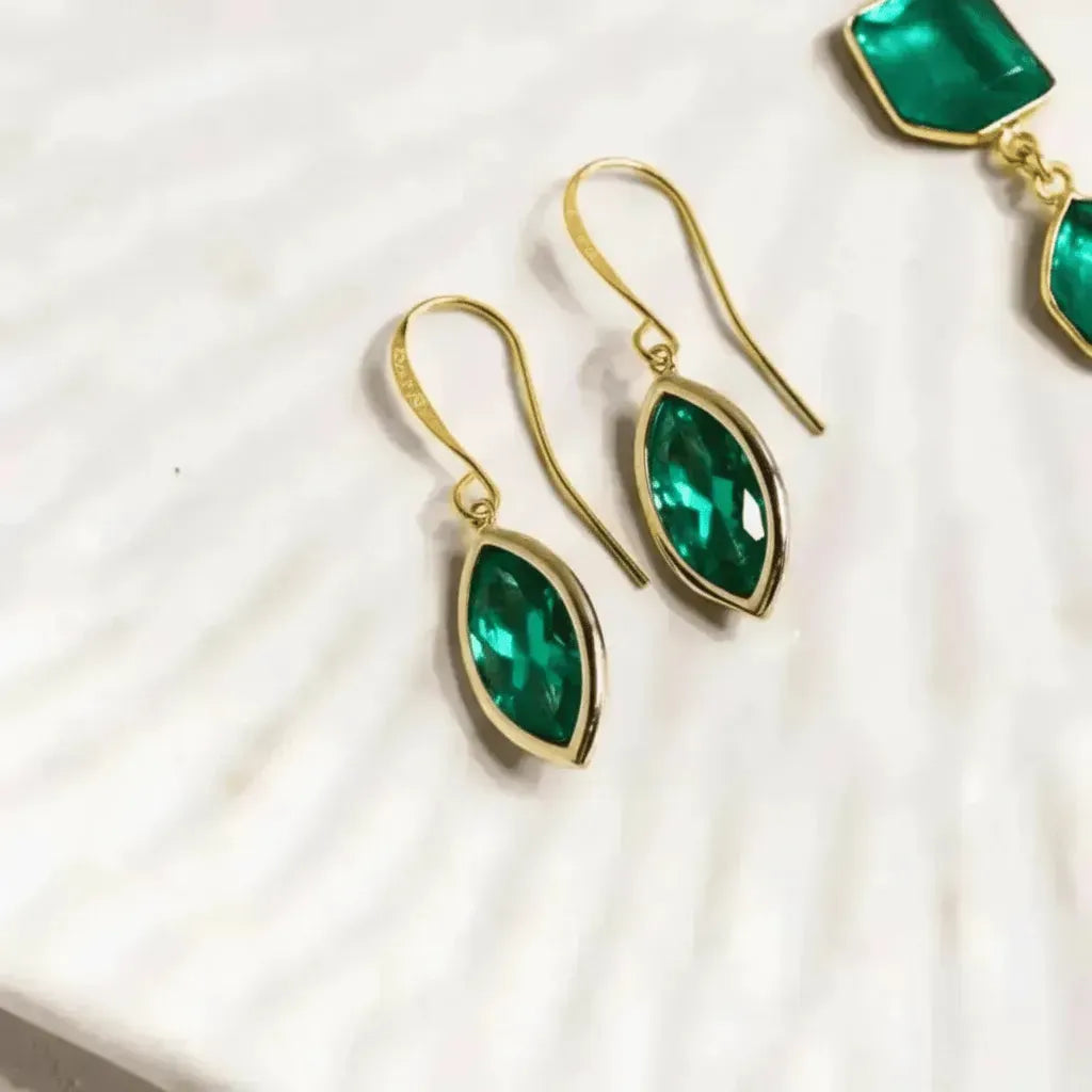 Gold earrings with green gemstones on a white fabric background