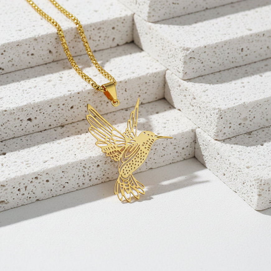Gold hummingbird pendant on a chain against a light textured background