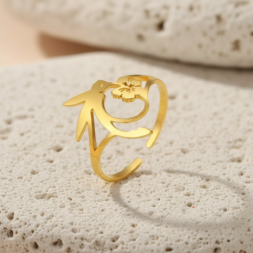 Gold hummingbird ring with floral design on a beige background
