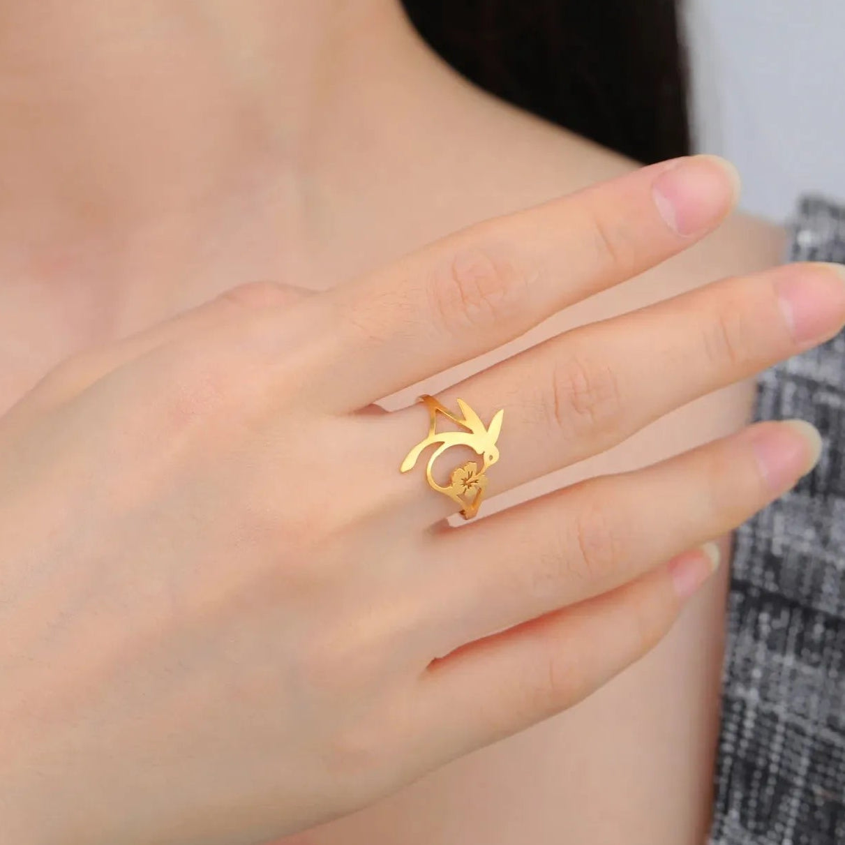 Gold hummingbird ring on a hand with a neutral background