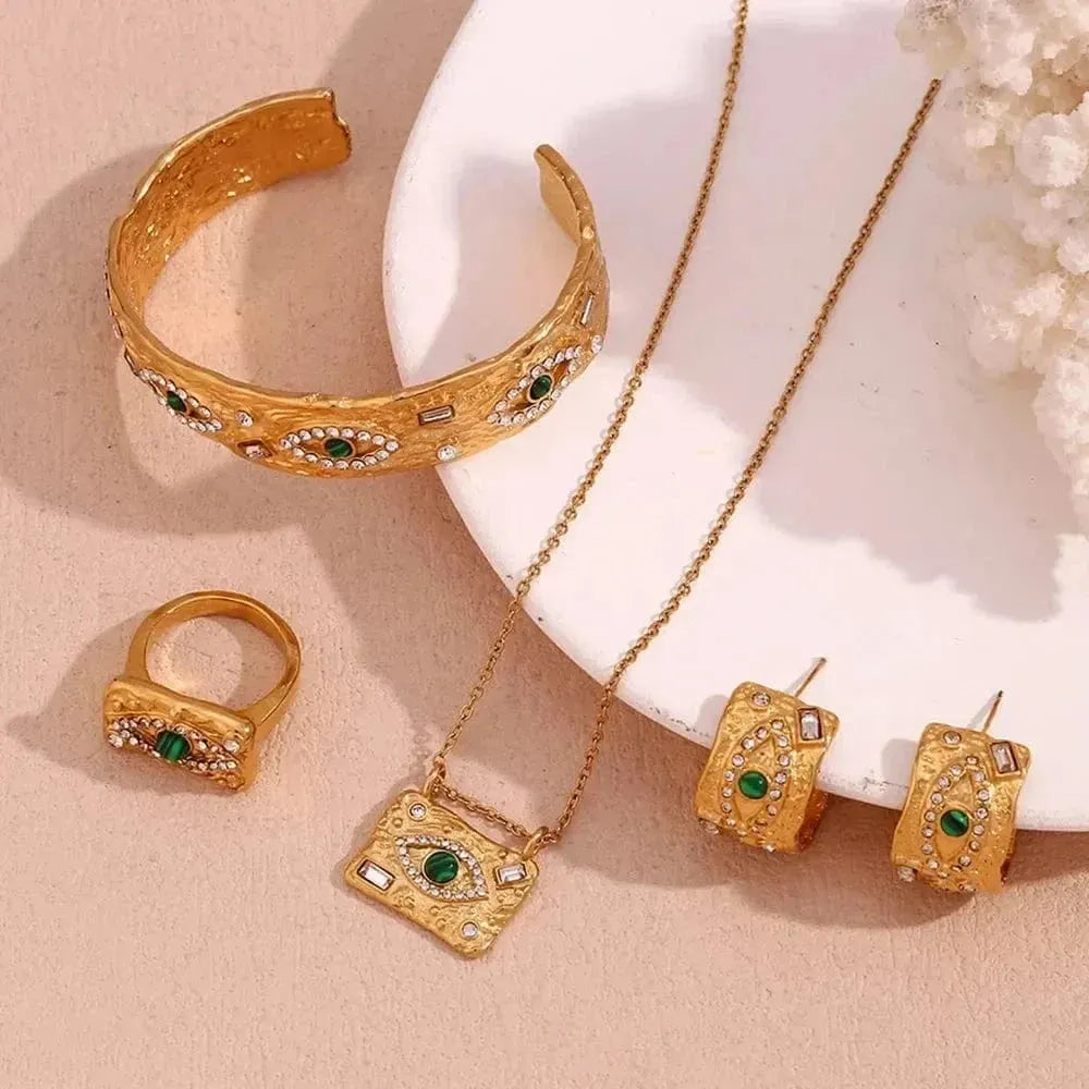 Gold jewelry set with bracelet, ring, necklace, and earrings on a beige background