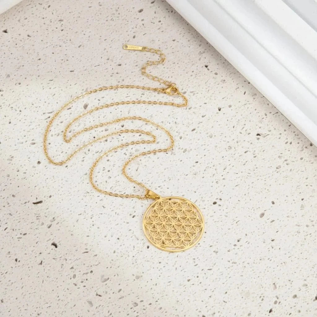 Gold necklace with a geometric pendant on a teal surface