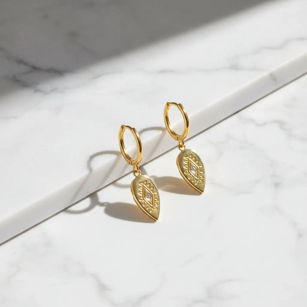 Gold hoop earrings with teardrop-shaped pendants on a white background 