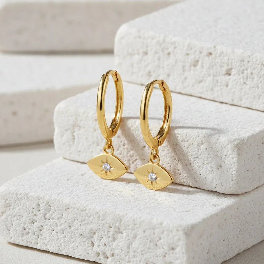 Gold hoop earrings with eye-shaped charms on a white background