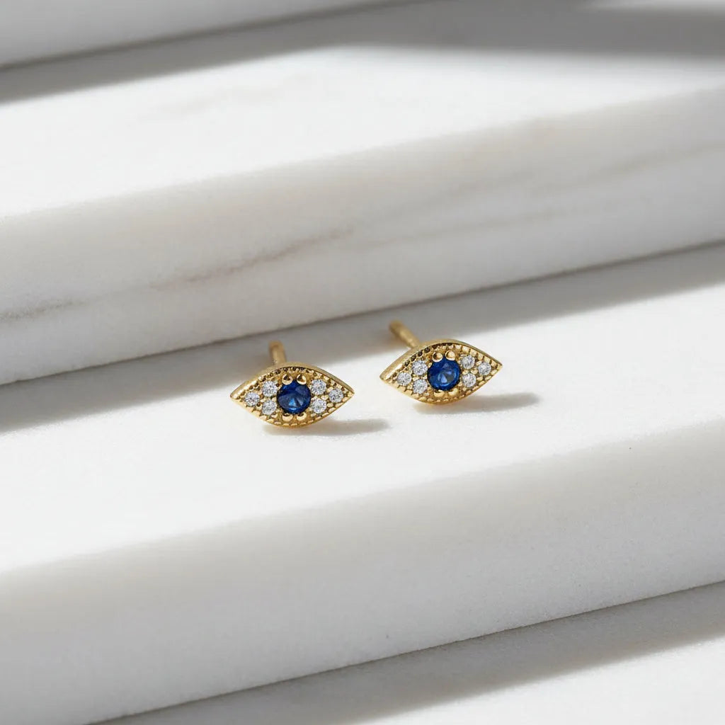 Gold eye-shaped earrings with blue gemstones on a white background