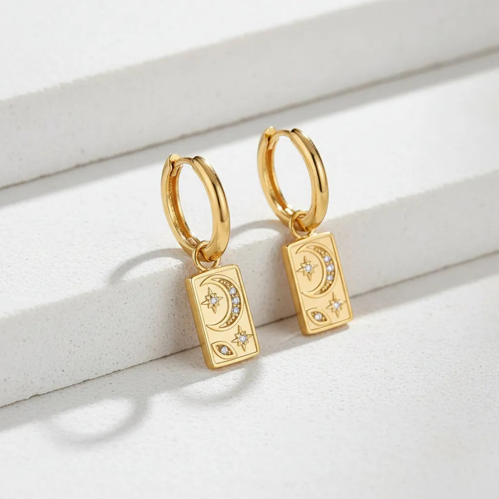 Gold hoop earrings with rectangular pendants featuring celestial designs on a white background.