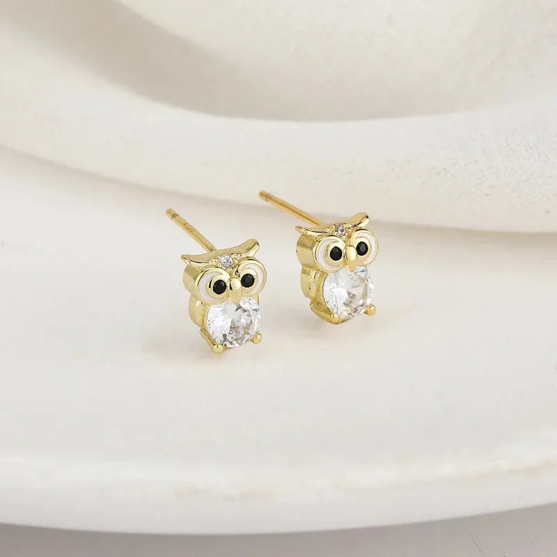 Gold owl-shaped earrings with clear gemstones on a beige background