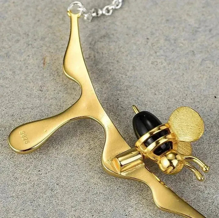 Gold bee-shaped pendant on a chain against a gray background