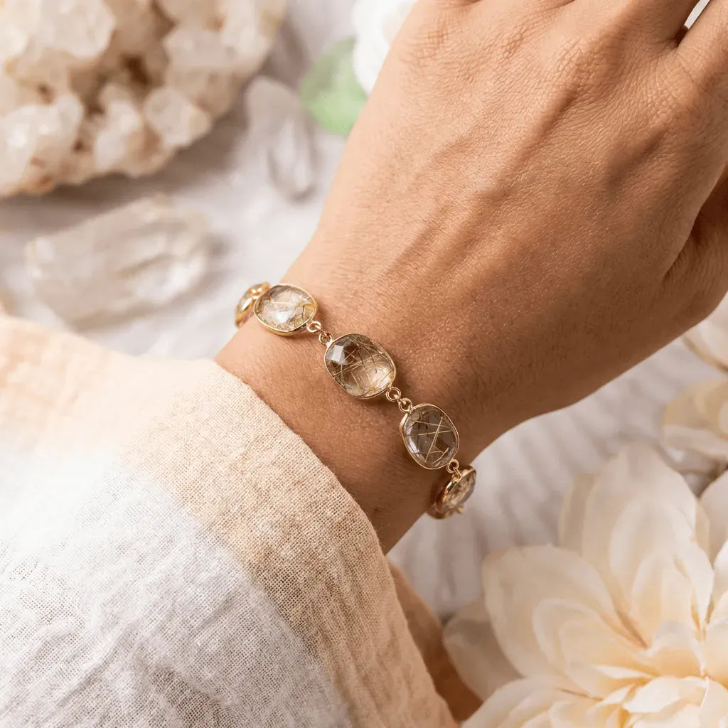 Gold bracelet with gemstones on a wrist, surrounded by flowers and crystals