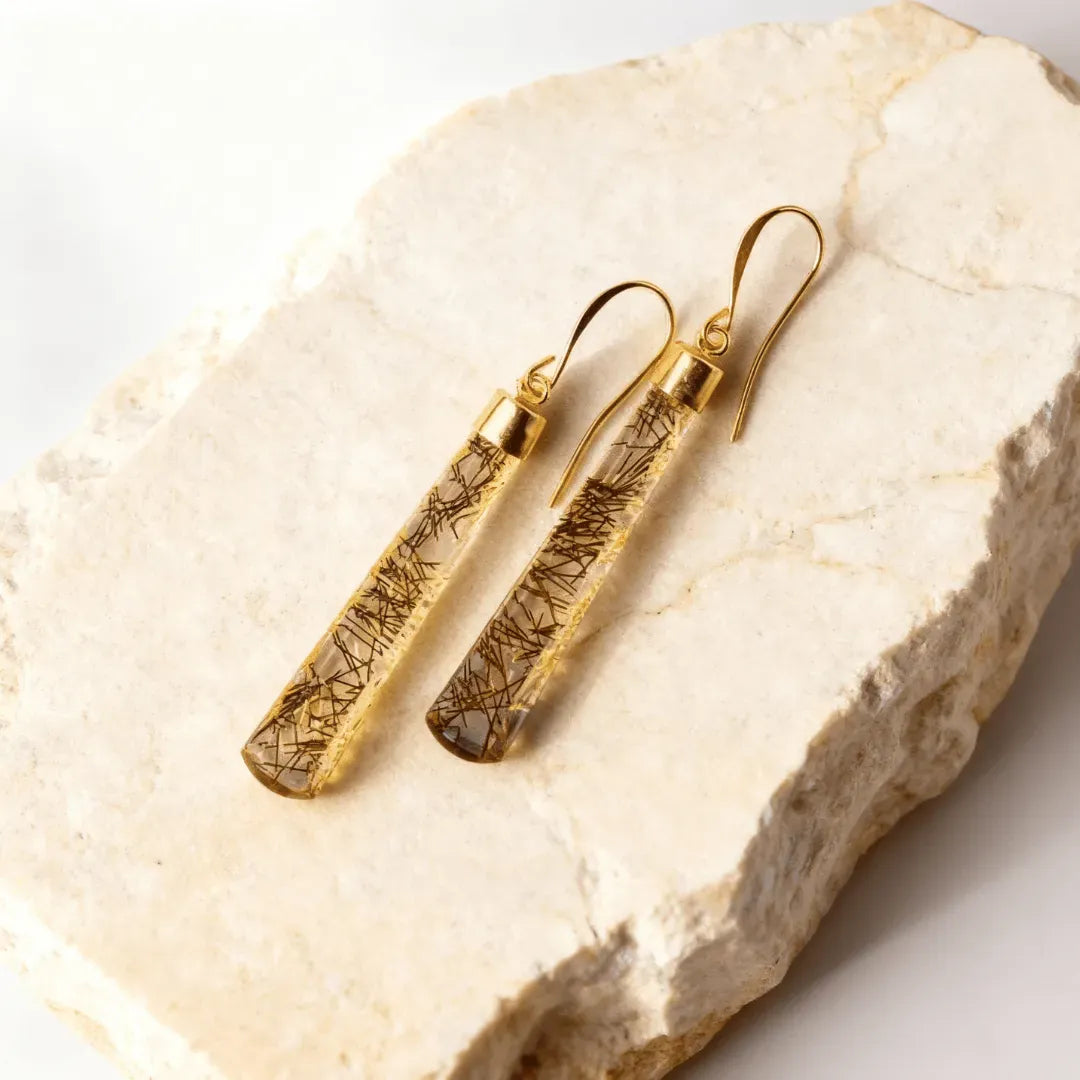 Gold earrings with embedded stones on a stone surface