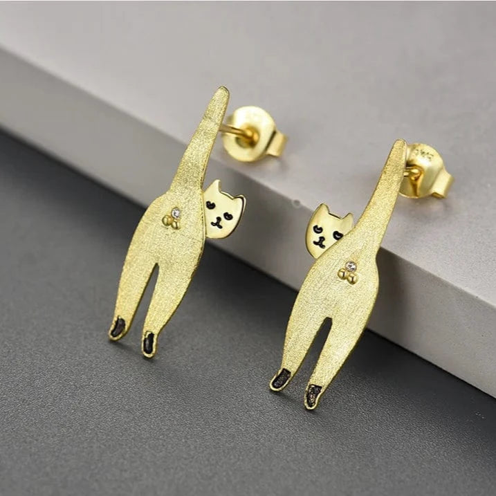 Gold cat-shaped earrings on a gray surface