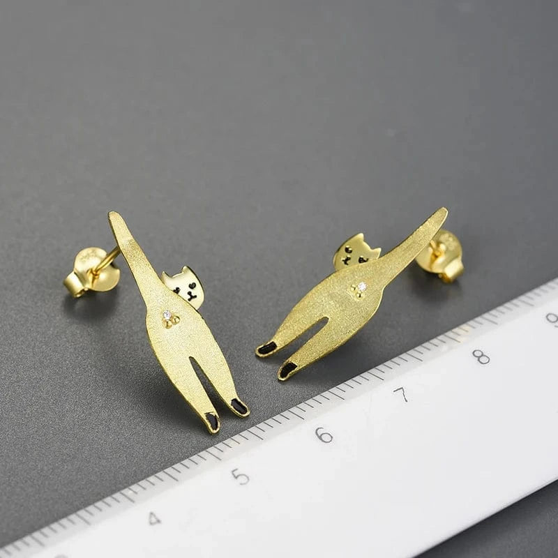 Gold cat-shaped earrings on a dark surface with a ruler for scale.