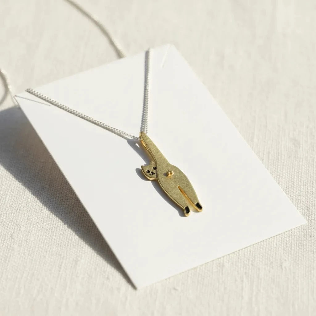 Gold necklace with a cat-shaped pendant on a white card against a beige background