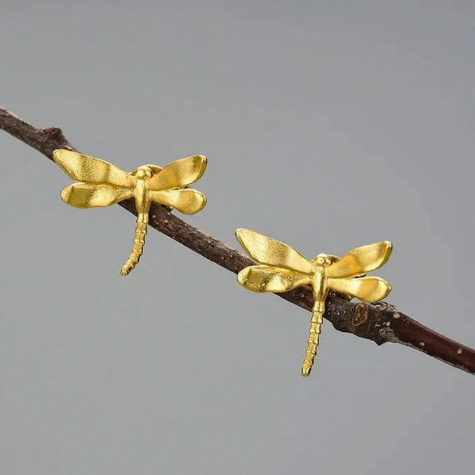 Gold dragonfly earrings on a branch with a gray background