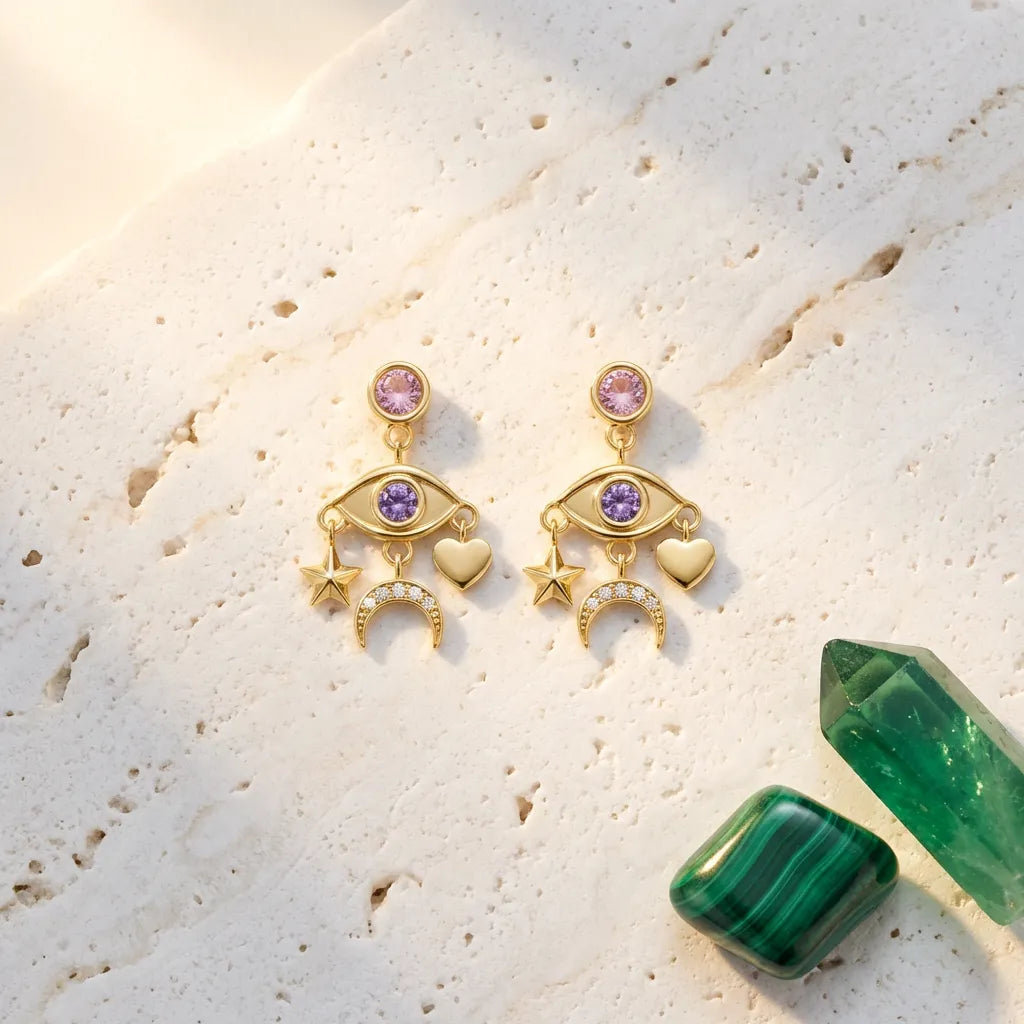 Gold earrings with gemstones on a textured surface with green crystals
