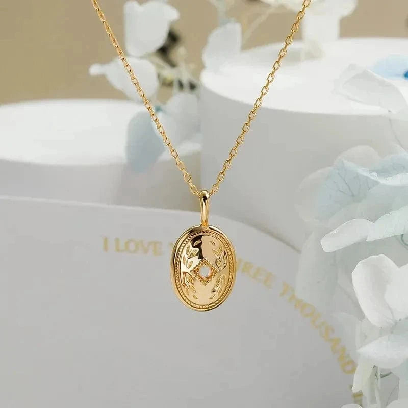 Gold necklace with a pendant on a white surface with floral decorations