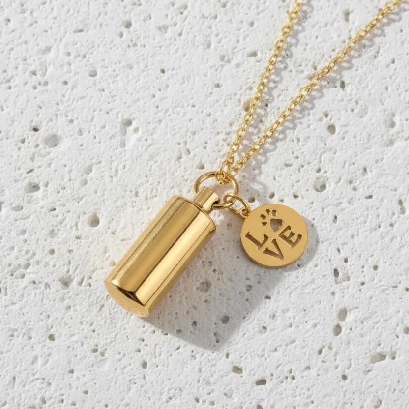 Gold necklace with a cylindrical pendant and a round tag on a white background