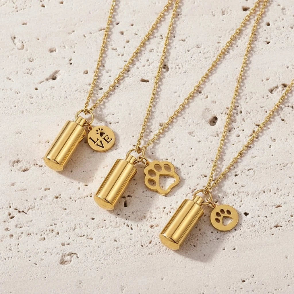 Three gold necklaces with cylindrical pendants and paw print charms on a black background
