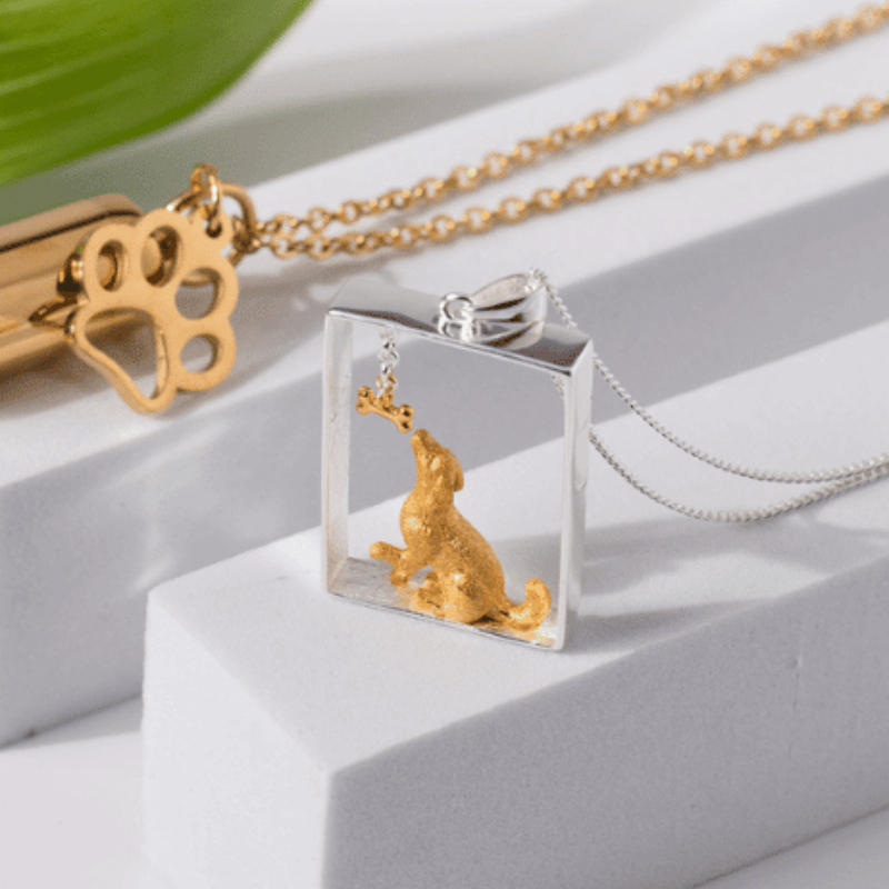 Sterling silver and gold dog portrait pendant on display with golden paw print charm, part of luxury pet jewelry collection.