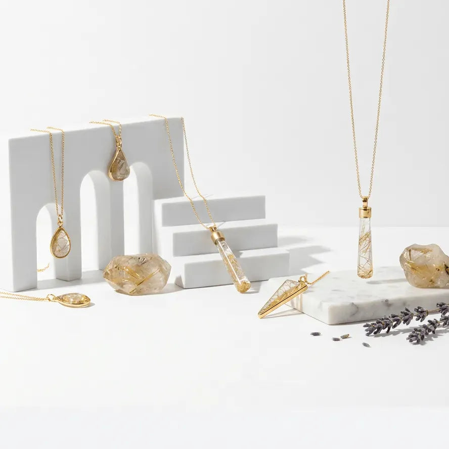 Gold necklaces on a white surface with decorative stones and lavender.