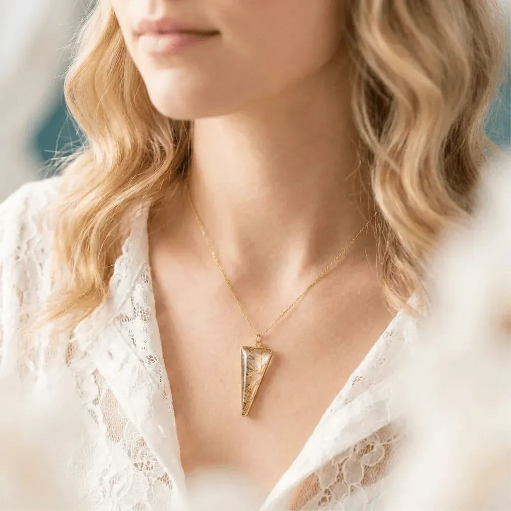 Gold necklace with a triangular pendant worn by a person in a white lace garment.