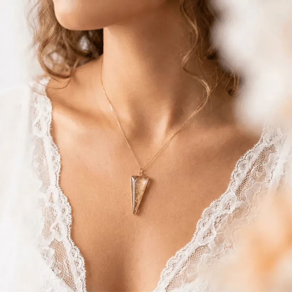 Gold necklace with a triangular pendant worn by a person in a lace garment.