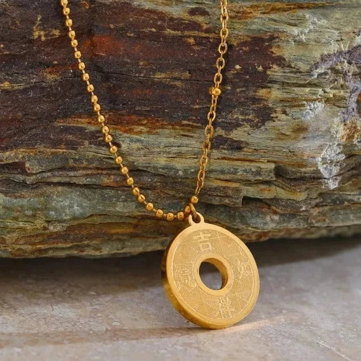 Gold necklace with a round pendant on a stone surface