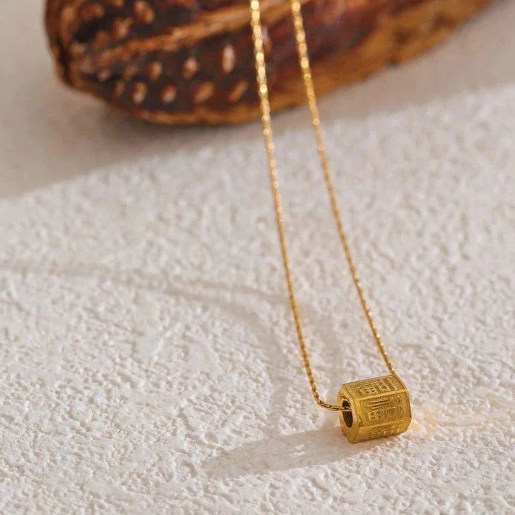 Gold necklace with a cube pendant on a textured surface