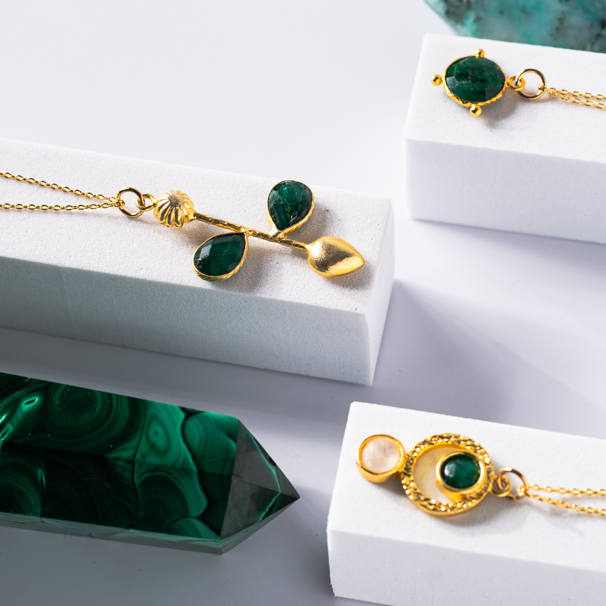 Gold-plated pendant necklace and matching earrings featuring brushed sacred geometry-inspired circle patterns. The pendant and earrings are adorned with vibrant emerald and luminous moonstone stones, symbolizing growth, intuition