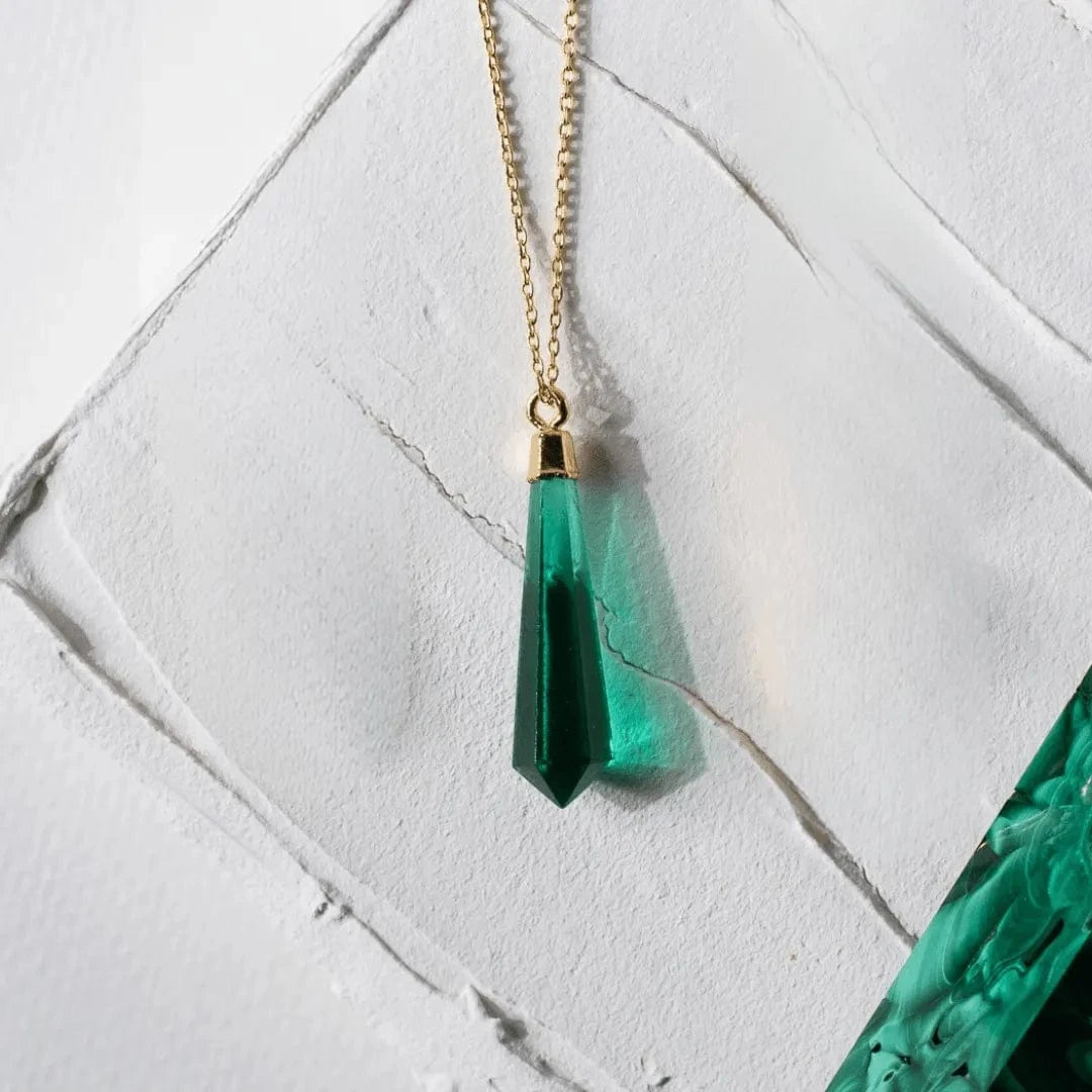 Green teardrop pendant necklace on a gold chain against a white marble background