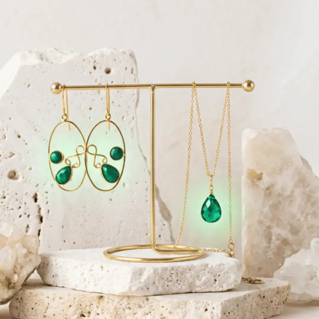 Gold earring and necklace set with green gemstones on a stone surface