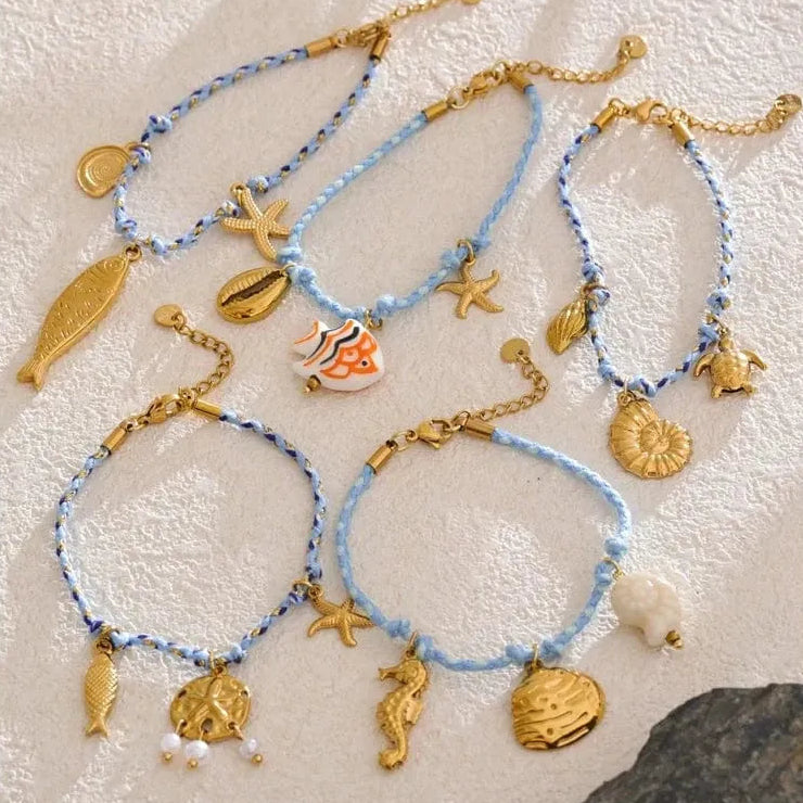 Set of beach-themed bracelets with charms on a textured surface
