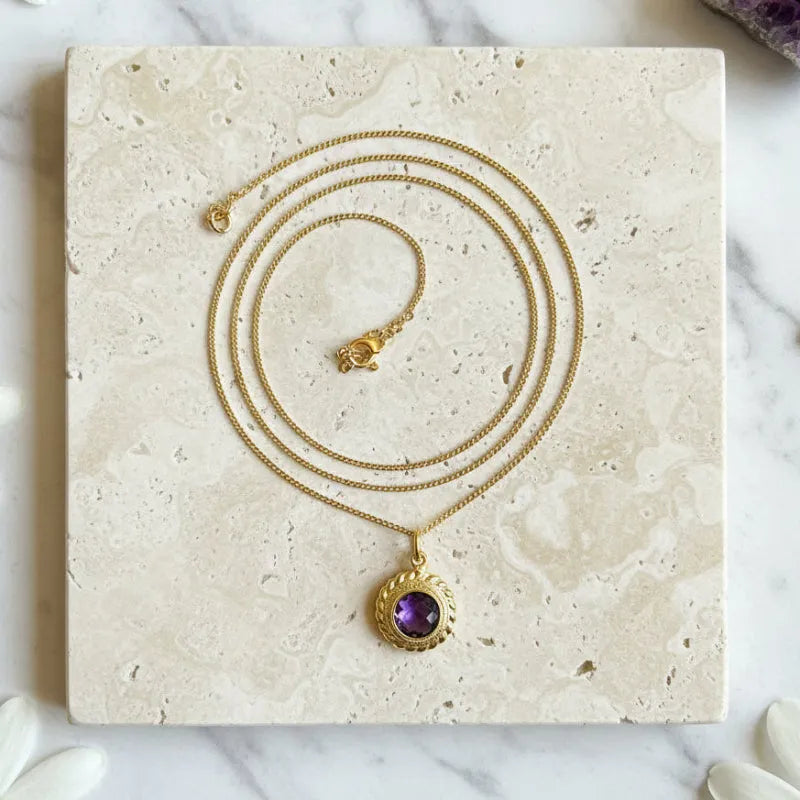 Amethyst Halo pendant necklace laid flat, purple stone ringed in etched gold