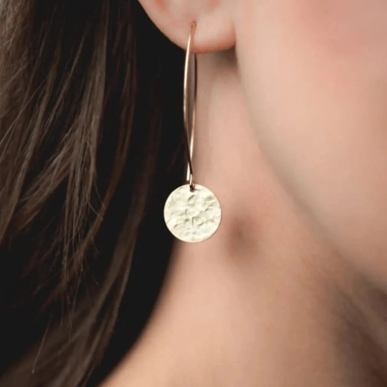 Gold earring worn by a person with blurred background