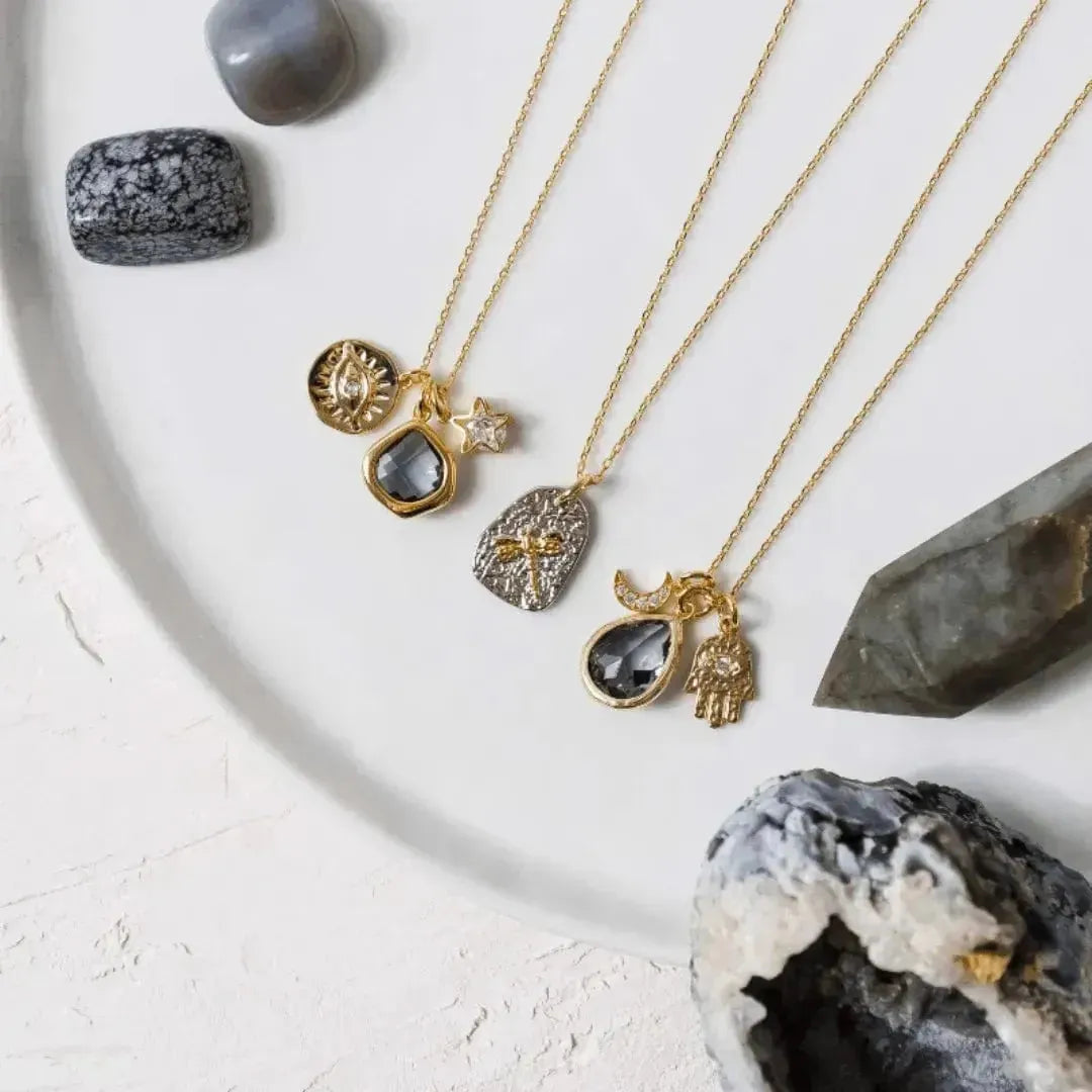 Gold necklaces with gemstone pendants on a white surface with crystals.