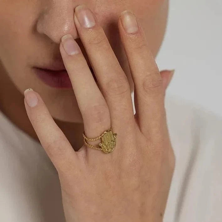 Close-up of a hand wearing a gold ring with a decorative design, against a neutral background.